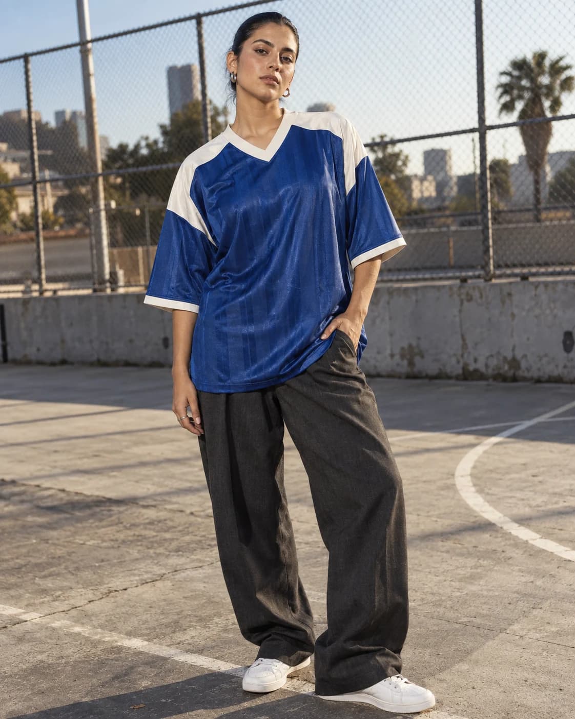 Model im kobaltblauen Retro-Trikot mit heller Schulterpartie und dunkler Stoffhose auf einem Sportplatz — KI-generiertes Beispiel